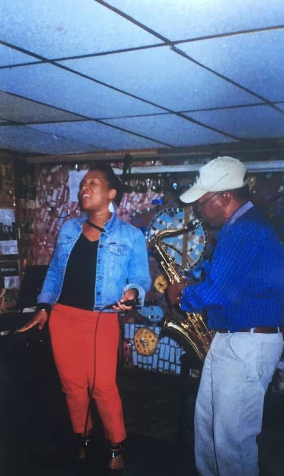 Christina Cunningham in a denim jacket singing beside a saxophonist