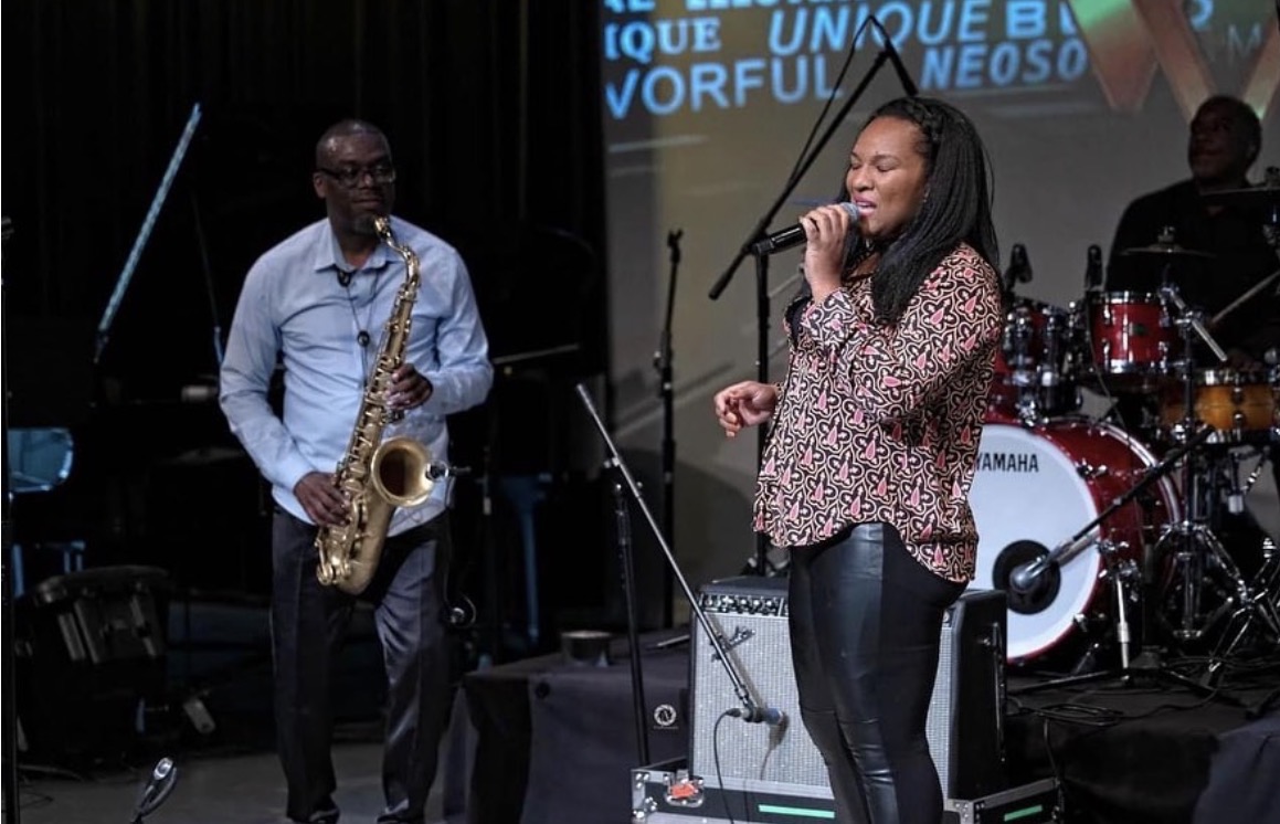 Christina Cunningham singing with a saxophonist and a drummer on an indoor stage