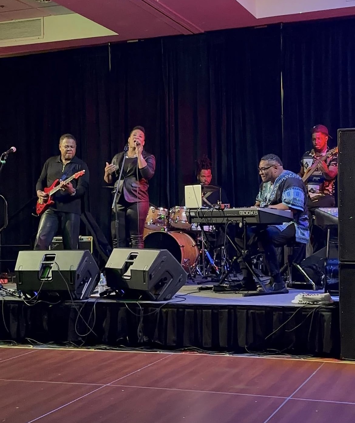 Christina Cunningham in black performing with a five-piece band on an event hall stage
