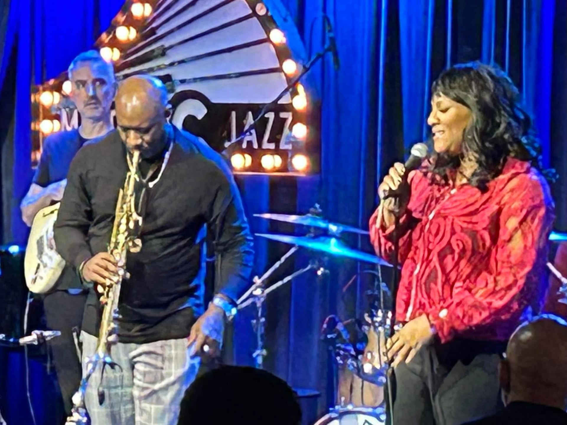 Christina Cunningham on stage with a saxophonist under a jazz club sign