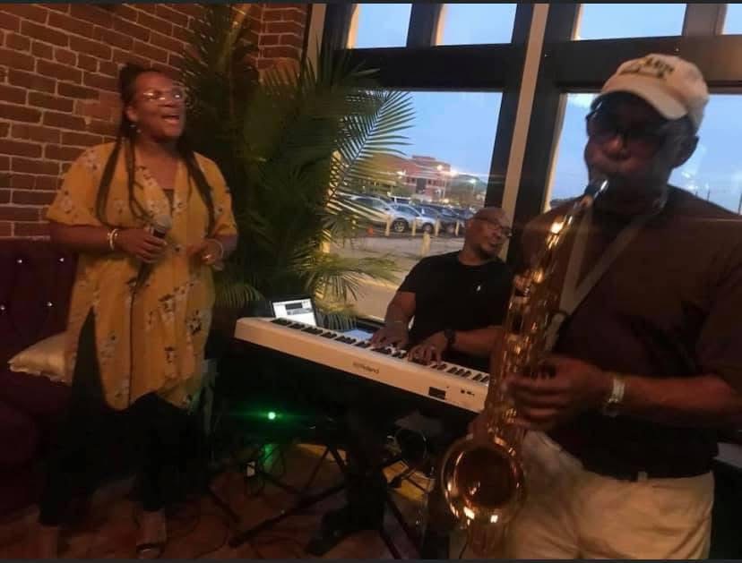Christina Cunningham singing beside a keyboardist and saxophonist at dusk