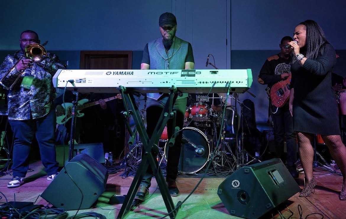 Christina Cunningham performing with a full band including a trombonist and keyboardist under blue stage lights