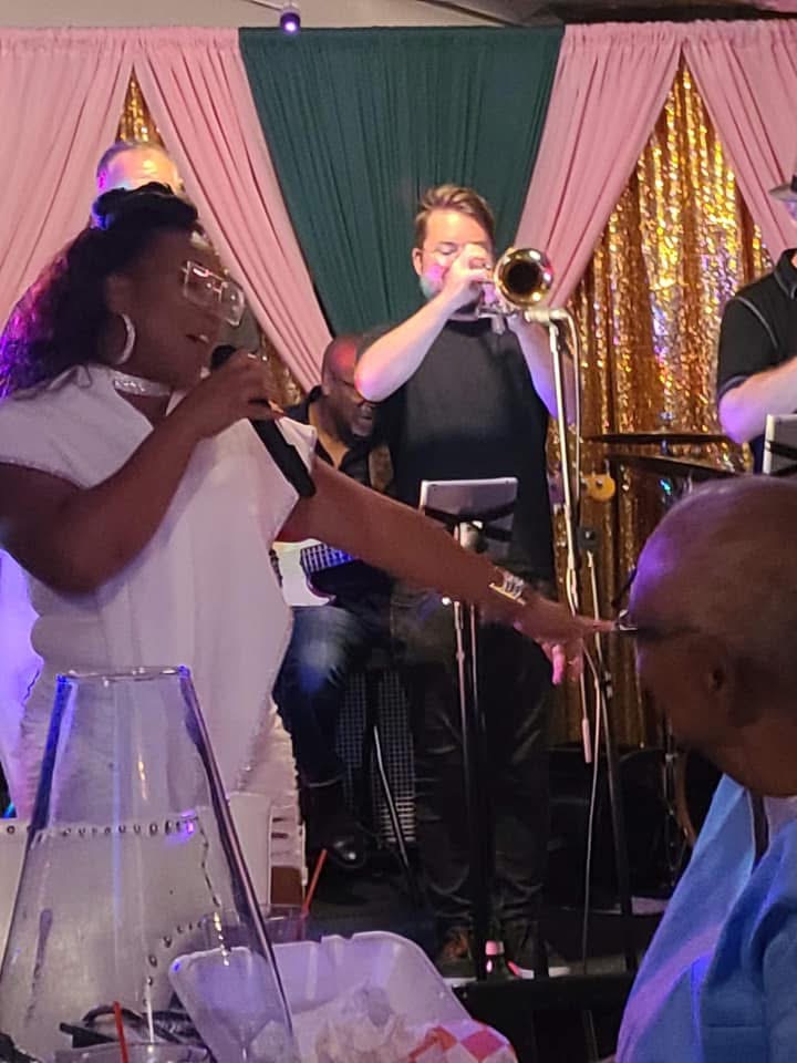 Christina Cunningham in white singing with a trumpeter on stage