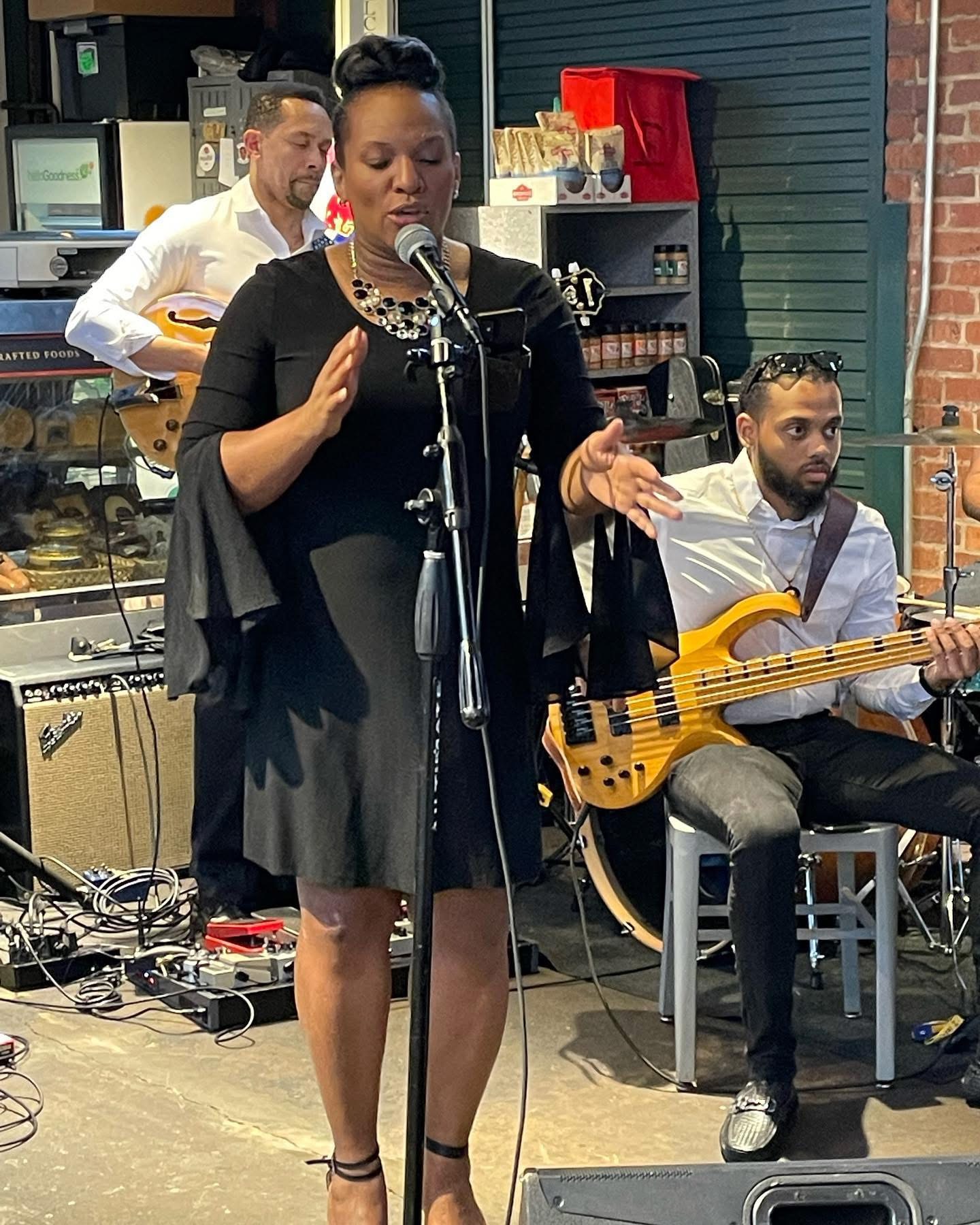 Christina Cunningham in a black dress singing with a guitarist and bassist
